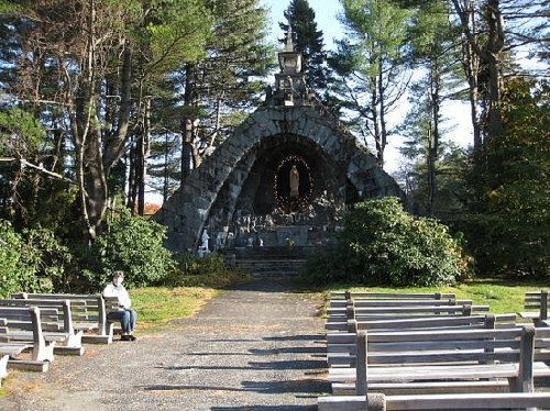 A stone structure resembling a chapel surrounded by trees, with wooden benches arranged in front.