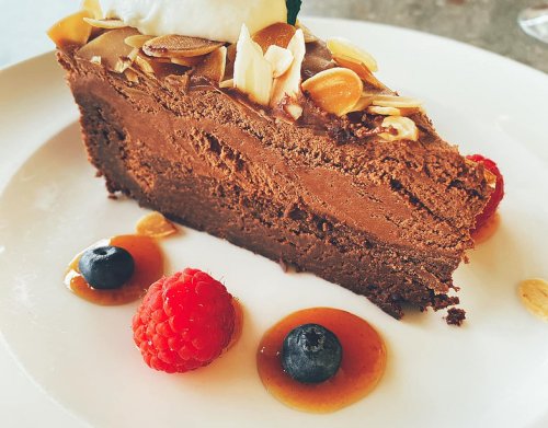 A slice of chocolate cake topped with almonds, served with raspberries and blueberries on a white plate.