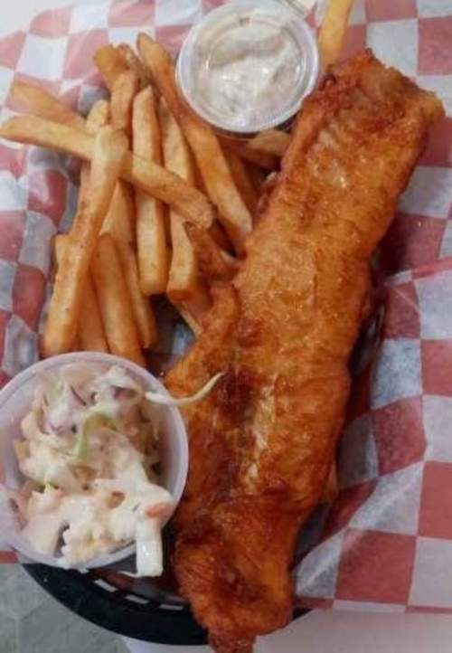 A plate of crispy fried fish with fries and coleslaw, served in a basket with checkered paper.