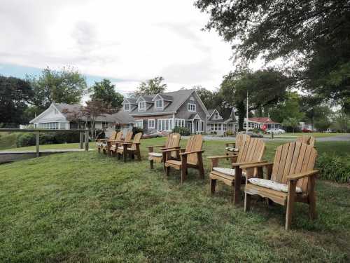 A row of wooden Adirondack chairs on a grassy area, with a house and trees in the background.