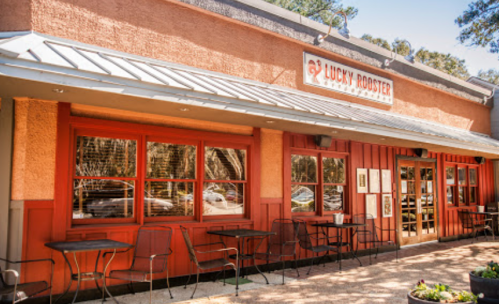 Exterior of Lucky Rooster restaurant with orange walls, large windows, and outdoor seating.