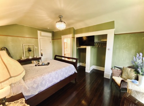 Cozy bedroom with a green wall, a bed, a TV, and a small seating area, featuring a chandelier and decorative accents.