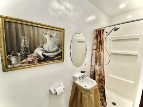 A bathroom featuring a shower, a small sink, a decorative painting, and a curtain with a floral pattern.