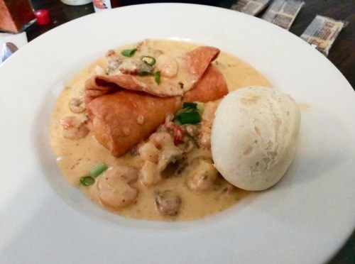 A plate featuring two crispy tortillas filled with shrimp in a creamy sauce, accompanied by a scoop of rice.