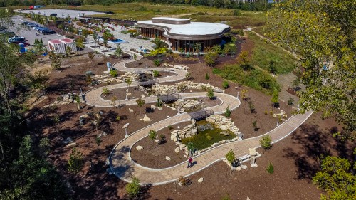 Aerial view of a landscaped area with winding paths, a pond, and a modern building surrounded by greenery.