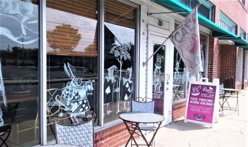 A café with artistic window murals, outdoor seating, and a flag announcing free parking.