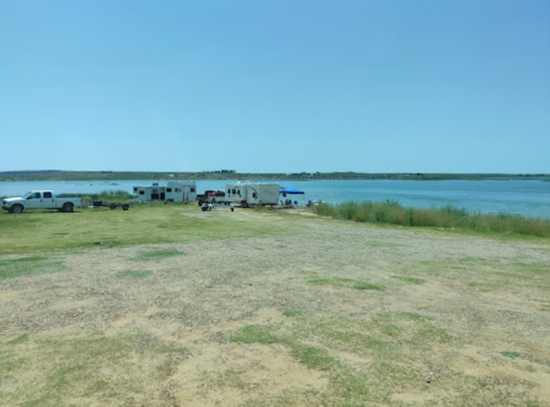 A serene lakeside scene with RVs parked on grassy land, surrounded by water and clear blue skies.