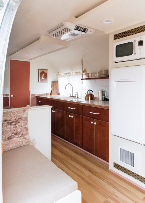 Cozy interior of a modern kitchen in a trailer, featuring wooden cabinets, a sink, and a small seating area.