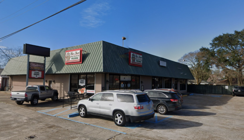 A small commercial building with a green metal roof, featuring several parked cars and a clear blue sky.