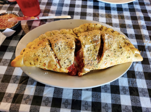 A large, golden-brown calzone with visible filling, served on a white plate on a black and white checkered tablecloth.