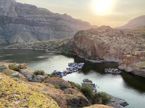 A serene landscape featuring a river surrounded by rocky cliffs and boats moored along the shore at sunset.