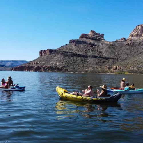 People kayaking on a calm lake surrounded by rocky hills and clear blue skies.