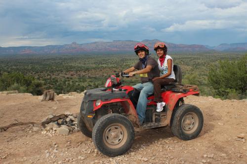 Two people on an ATV in a scenic landscape with mountains and greenery under a cloudy sky.