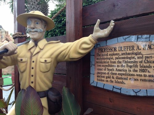 A statue of a smiling explorer in a tan outfit, gesturing beside a sign about Professor Duffer A. Fac.
