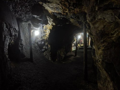 Dimly lit underground cave with rocky walls and wooden supports, featuring two lights illuminating the path ahead.