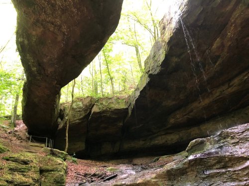 A serene cave with a large overhang, surrounded by lush greenery and a small waterfall cascading down the rocks.