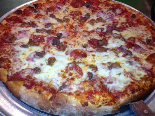 A large pizza topped with pepperoni, sausage, ham, and melted cheese on a golden crust.