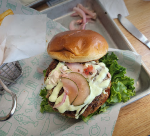 A close-up of a burger with lettuce, pickles, tomatoes, and creamy sauce on a toasted bun, served on a tray.