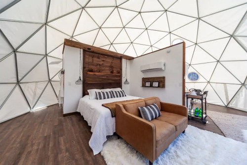 Cozy interior of a geodesic dome featuring a bed, a sofa, and modern decor with wooden accents.