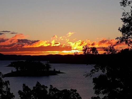 A vibrant sunset over a lake, with colorful clouds and silhouettes of trees and an island in the foreground.