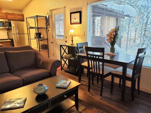 Cozy living space featuring a sofa, dining table, and large window with a view, decorated with flowers and warm lighting.
