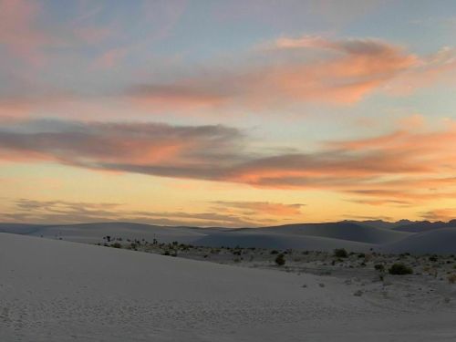 A serene desert landscape at sunset, featuring soft pink and orange clouds over white sand dunes.