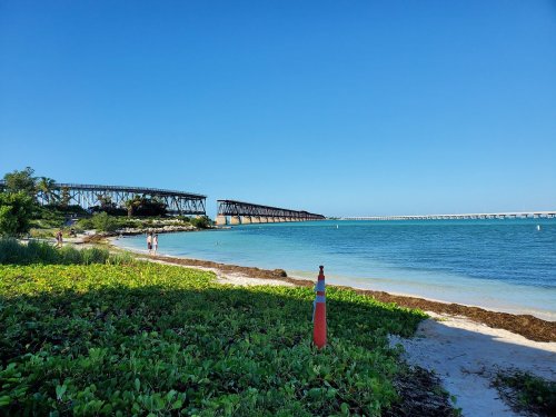 A scenic view of a beach with a railway bridge in the background and clear blue skies.