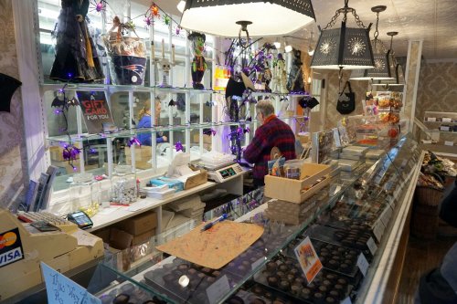 A cozy shop display with Halloween decorations, showcasing treats and a cashier assisting a customer.