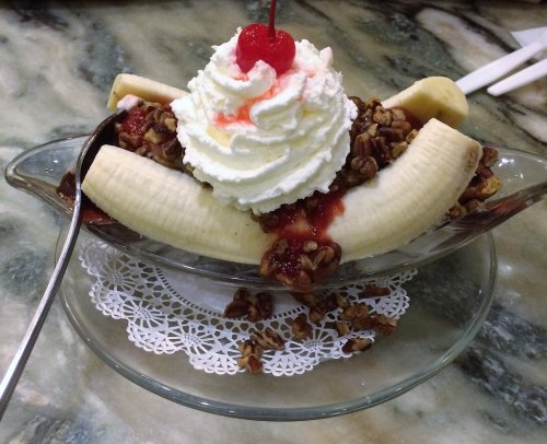 A banana split topped with whipped cream, a cherry, nuts, and strawberry sauce in a glass dish.