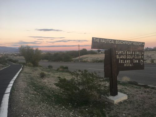 Sign for The Nautical Beachfront Resort with directions to Turtle Bar & Grill, Island Link Golf, and hotel at sunset.