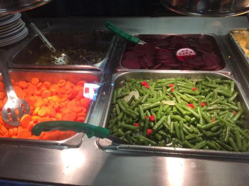 A buffet display featuring trays of carrots, green beans, and beets with serving utensils.