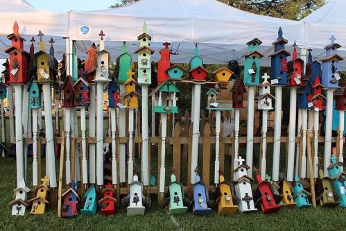 A colorful display of various birdhouses arranged on a wooden stand under a white tent.