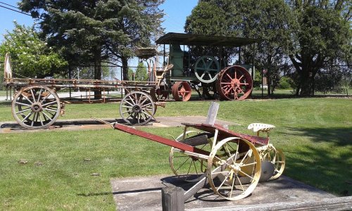 Historic agricultural equipment displayed on a grassy area, featuring a cart and a vintage tractor in the background.
