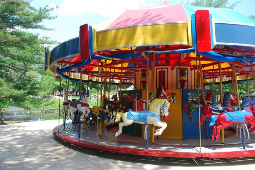 A colorful carousel with painted horses, set in a park surrounded by trees on a sunny day.