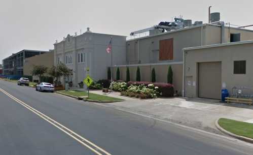 Street view of a building with an American flag, surrounded by greenery and parked cars.