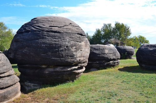Large, round boulders with textured surfaces scattered across a grassy area under a blue sky.