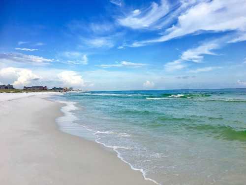 A serene beach scene with soft white sand, gentle waves, and a bright blue sky with scattered clouds.