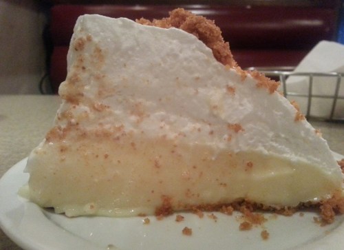 A slice of creamy pie topped with whipped cream and crumbled graham cracker crust on a white plate.