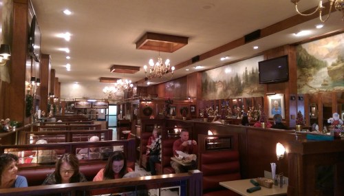 A cozy diner interior with wooden booths, chandeliers, and patrons enjoying meals in a warm, inviting atmosphere.