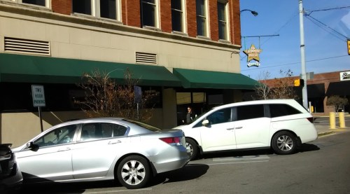 A silver car and a white minivan parked outside a building with green awnings on a sunny day.
