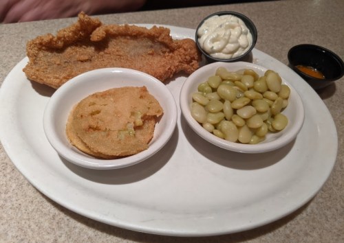 A plate featuring fried fish, a cornbread patty, green beans, and a small cup of coleslaw.