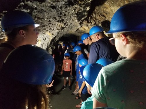 A group of people wearing blue helmets inside a dimly lit cave, exploring the rocky surroundings.