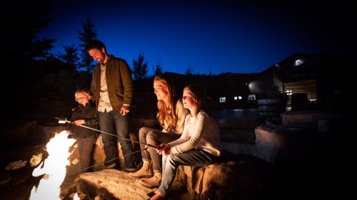 A group of four people gathered around a campfire at night, roasting marshmallows and enjoying the outdoors.