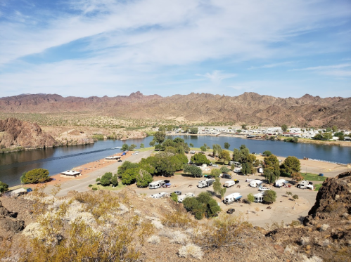 A scenic view of a river surrounded by mountains, with a campground featuring RVs and trees along the shore.