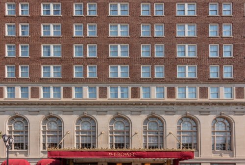 Facade of a historic hotel with brick exterior and large arched windows, featuring a red awning at the entrance.