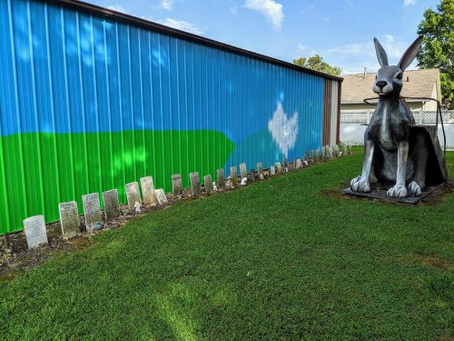 A large rabbit statue beside a row of gravestones, with a colorful mural on the wall in the background.