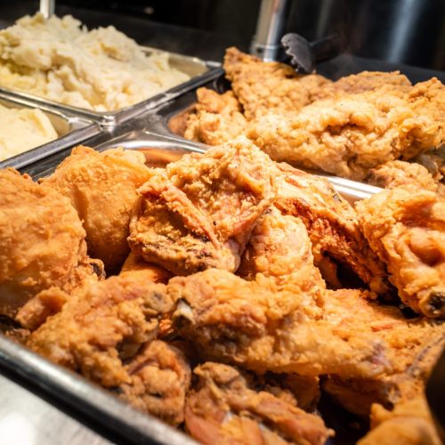 A close-up of crispy fried chicken pieces in a serving tray, with mashed potatoes in the background.