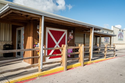 A wooden barn-style building with a red door and cartoon animal decorations, surrounded by a wooden fence.