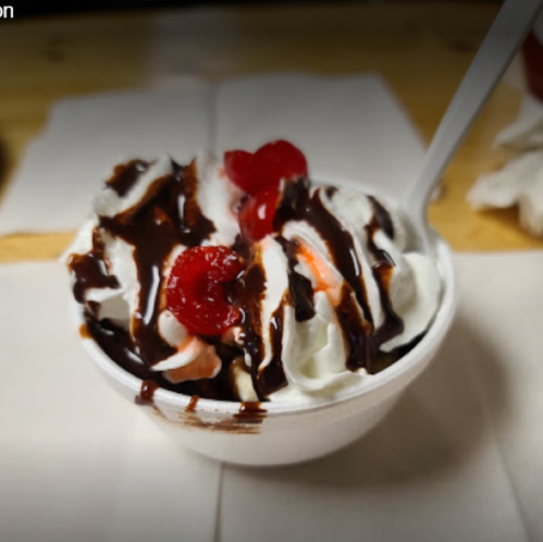 A dessert bowl filled with ice cream, topped with whipped cream, chocolate sauce, and cherries.