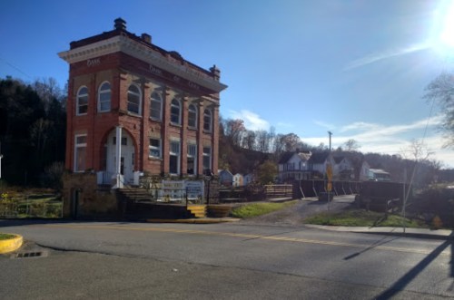 Historic red brick building with large windows, set against a clear blue sky and trees in the background.
